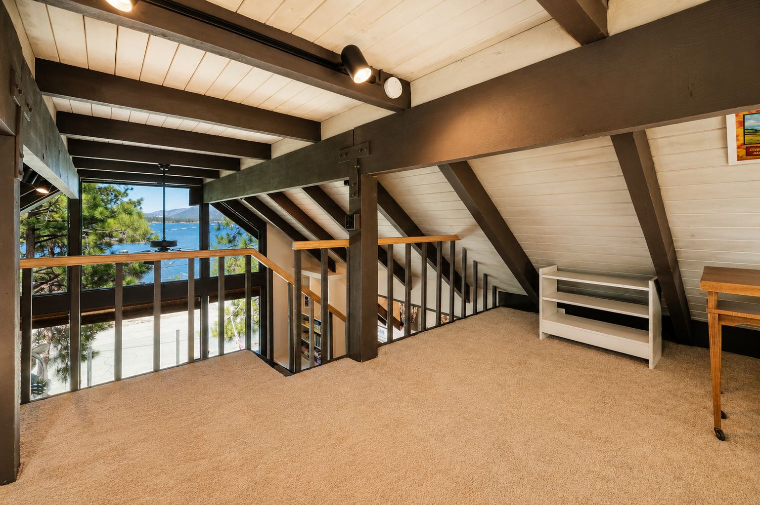 Une pièce spacieuse située sous les toits, avec un plafond en pente, un escalier en bois et une vue sur l’extérieur.