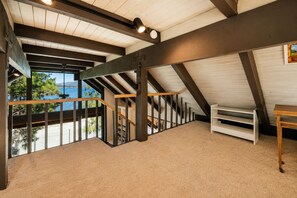 Une pièce spacieuse située sous les toits, avec un plafond en pente, un escalier en bois et une vue sur l’extérieur.