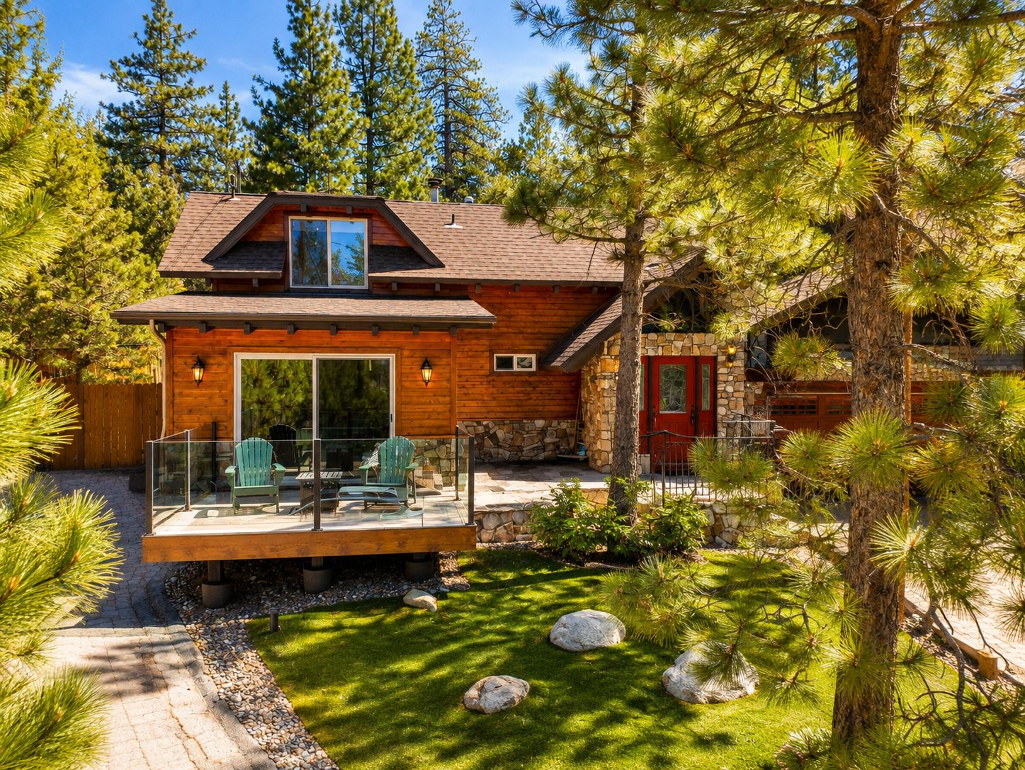 A cabin with a deck, stone walls, and a red door.