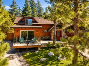 A cabin with a deck, stone walls, and a red door.