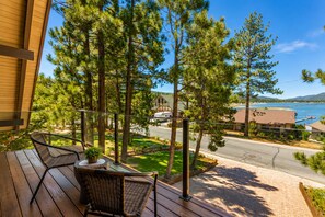 A balcony with wicker furniture, a potted plant, and a view of a road, trees, and a body of water.