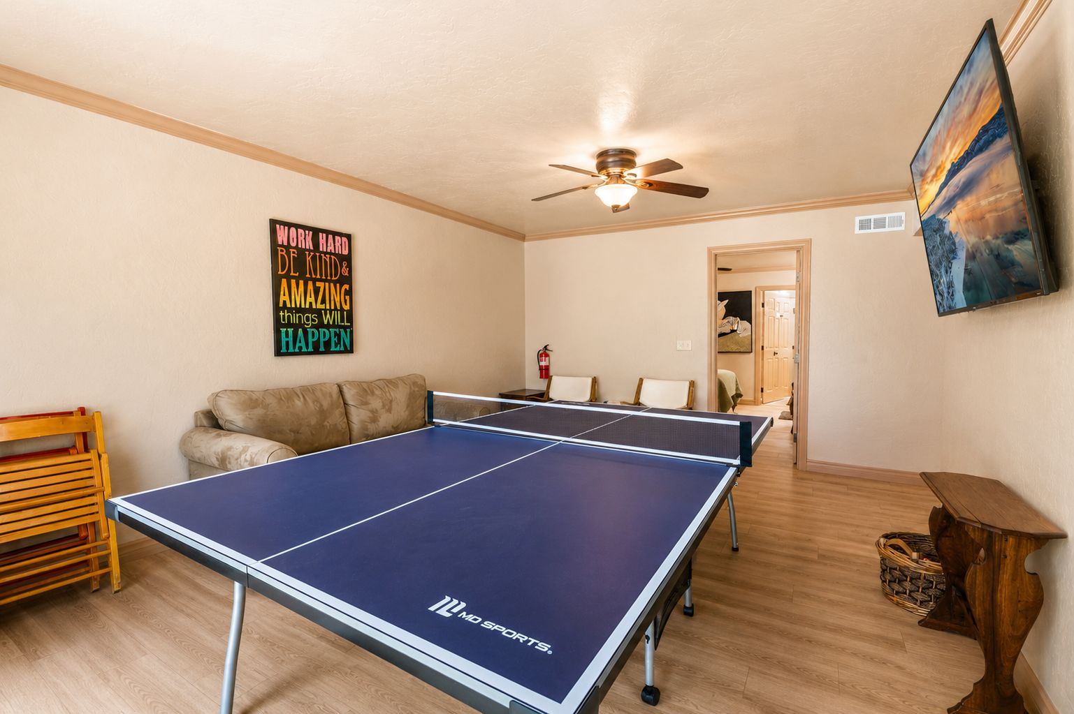 Een ruimte met twee pingpongtafels, een plafondventilator en een motiverende poster aan de muur.
