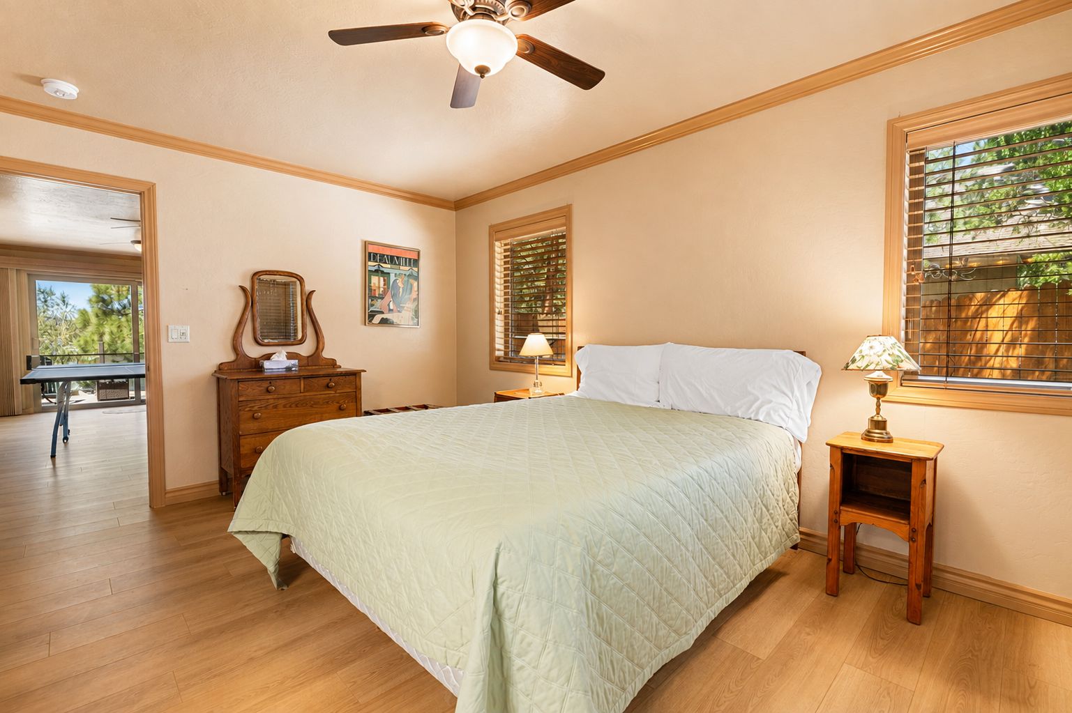 A bedroom with a bed, a ceiling fan, a dresser, a nightstand, and a window with blinds.