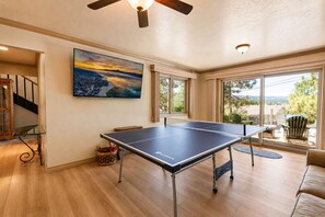 A room with a ping pong table, a painting, and a view of the outdoors.