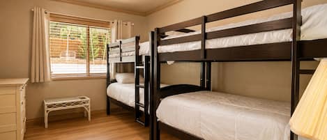 A bunk bed room with a ceiling fan, a window with curtains, a small bench, and a bedside table.