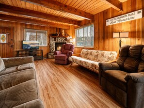 A cozy living room with wooden walls, a fireplace, a television, and comfortable seating.
