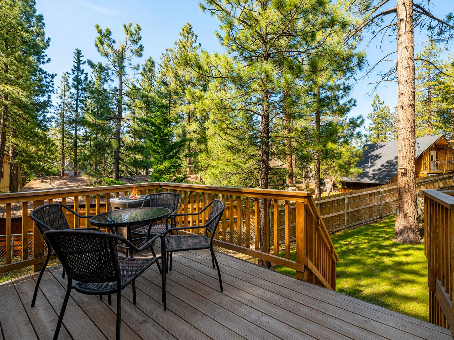A wooden deck with a table and chairs, surrounded by tall pine trees.