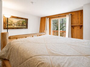 A bedroom with a large bed, wooden headboard, a painting on the wall, and a window with curtains.