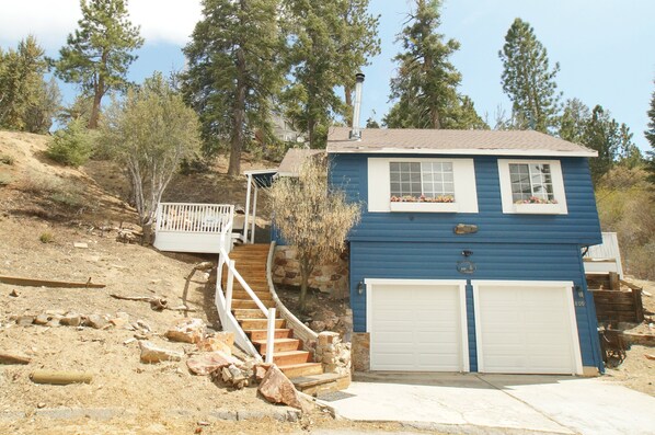 A two-story blue house with a stone staircase, a white porch, and a garage.