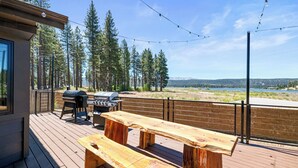 Terraza exterior con bancos de madera y una parrilla de barbacoa, con vistas a un lago y un bosque.