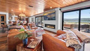 Un salón amplio con sofás de cuero, chimenea y ventanas grandes que ofrecen vistas al exterior.