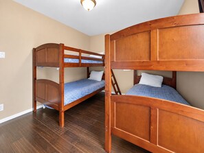 A room with two bunk beds, wooden flooring, and a ceiling light fixture.