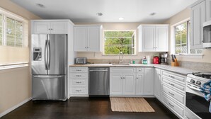 Cocina moderna con armarios blancos, electrodomésticos de acero inoxidable y ventana con vistas a la vegetación.