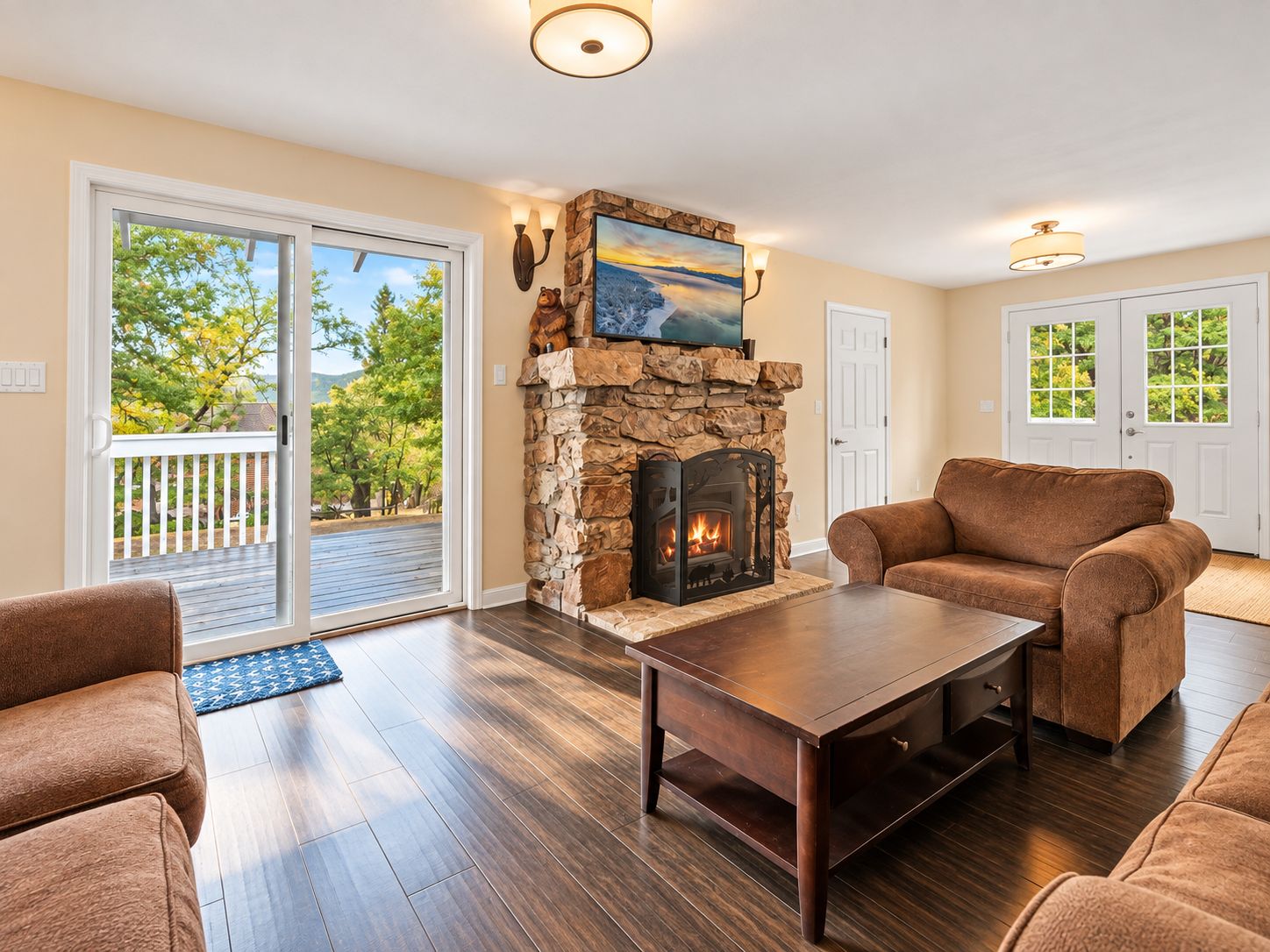A living room with a stone fireplace, a sofa, a coffee table, and a view through a glass door.
