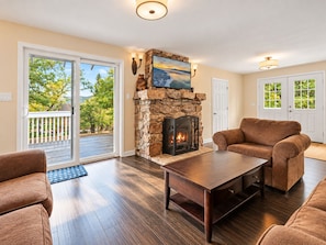 A living room with a stone fireplace, a sofa, a coffee table, and a view through a glass door.