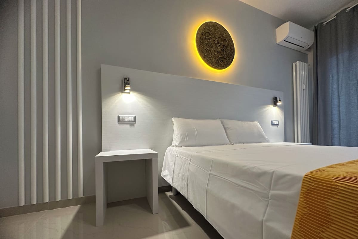 A modern hotel room with a large bed, a bedside table, and a wall-mounted air conditioning unit.