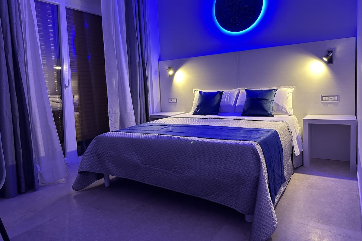 A modern bedroom with a bed, nightstands, and a circular light fixture on the wall.