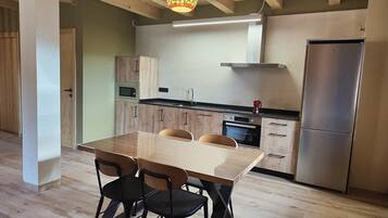 Una cocina moderna con armarios de madera, un refrigerador de acero inoxidable, una mesa de comedor con sillas y una lámpara colgante.