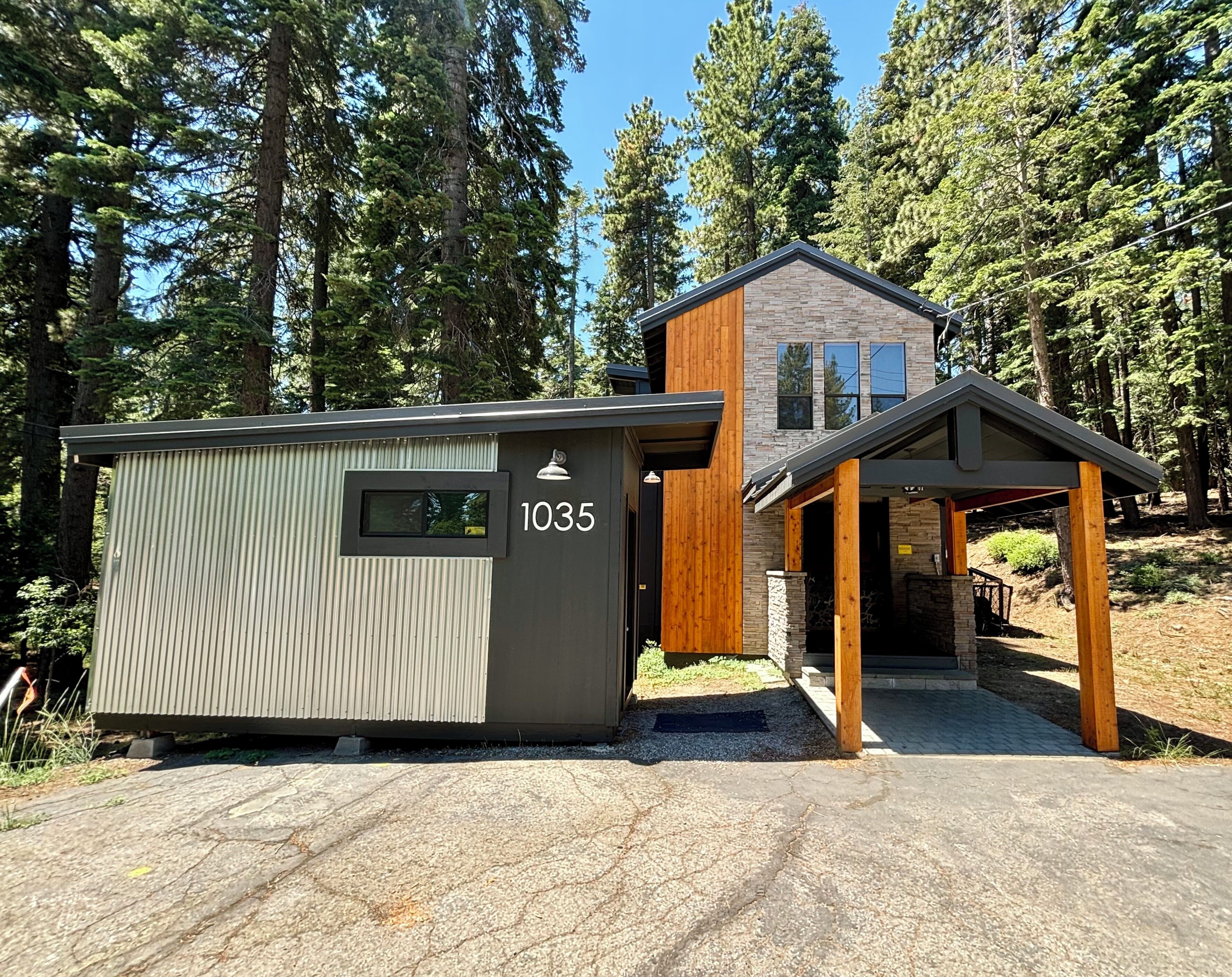 A modern cabin with a small attached shed, surrounded by a forest.