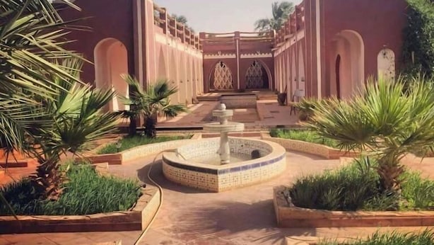 A courtyard with a central fountain, surrounded by palm trees and a building with arches. - Hotel Tin Habib (Timimoun)