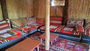 A traditional room with a thatched roof, a sofa set with patterned cushions, and a wooden bench. - Hotel Tin Habib (Timimoun)