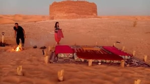 A desert scene with a fire, a tent, and a large rock formation in the background. - Hotel Tin Habib (Timimoun)