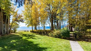 A pathway leading to a lake with trees displaying autumn foliage, a grassy area, and a building on the left. - St Francis Townhome with Amenities, near the lake (Tahoe City)