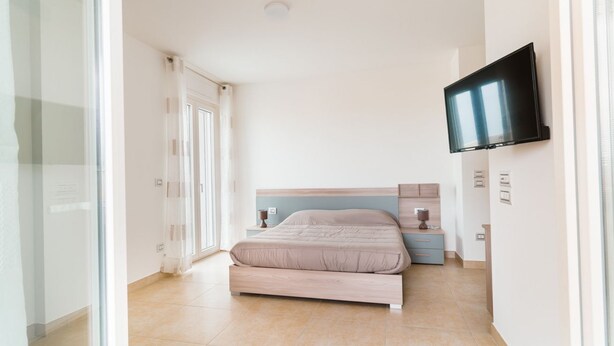 A bedroom with a bed, a TV mounted on the wall, a bedside table, and a window. - GuestHost - Scaringi Palace Trani - Room 1B (Trani)
