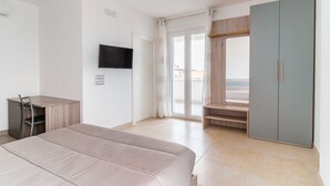 A bedroom with a bed, a desk, a wardrobe, a television, and a sliding door to a balcony. - GuestHost - Scaringi Palace Trani - Room 1B (Trani)