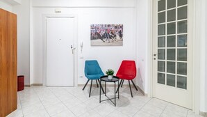 Ein Zimmer mit weißer Tür, einem kleinen Tisch mit zwei Stühlen, einem Bild an der Wand und einem Fenster mit satinierten Scheiben.