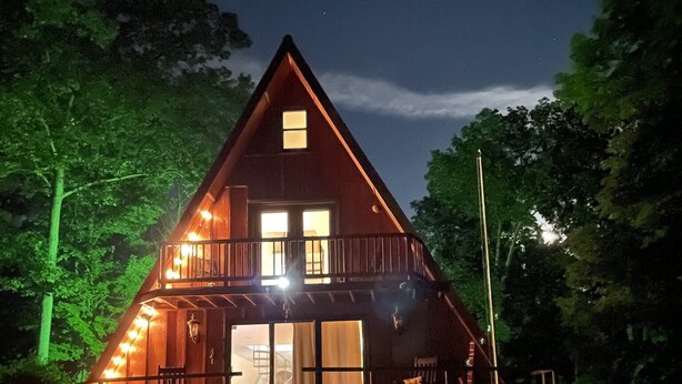 A wooden cabin with a balcony, large windows, and a staircase leading to the entrance. - Wild Ivy Cottage A-Frame (Rockville)