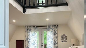 A bedroom with a large bed, a wooden floor, a staircase, and a door. - Wild Ivy Cottage A-Frame (Rockville)