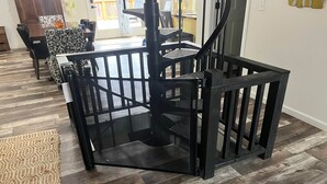A modern interior with a black metal staircase, a patterned rug, and a dining area with chairs and a table. - Wild Ivy Cottage A-Frame (Rockville)