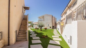 Un patio estrecho con una escalera, un árbol y un edificio con balcones.