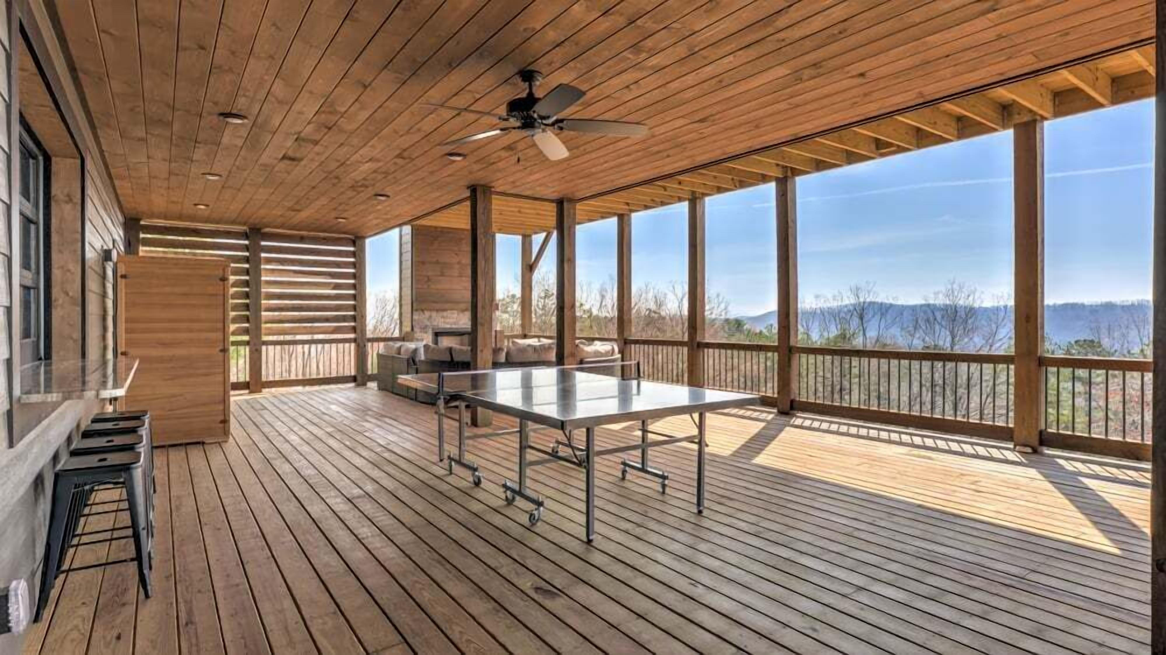 A covered outdoor deck with a table and chairs, large windows, and a view of the landscape.