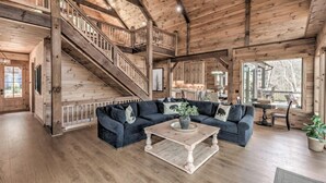 A spacious living room with a dark blue sectional sofa, a wooden coffee table, and a staircase leading to an upper level.