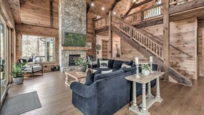 A spacious living room with a stone fireplace, a large sofa, and a wooden staircase.