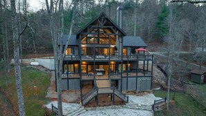 A multi-story log cabin with a stone staircase leading to the entrance, surrounded by trees.