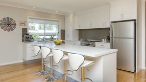 A modern kitchen with white cabinets, a stainless steel refrigerator, a central island with bar stools, and a coffee machine. - Beautiful Vibe Energy Escape Lux w Bonuses Phillip Island 100m to nature inlet (Rhyll)