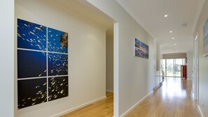 A hallway with wooden flooring, white walls, and artwork. - Beautiful Vibe Energy Escape Lux w Bonuses Phillip Island 100m to nature inlet (Rhyll)