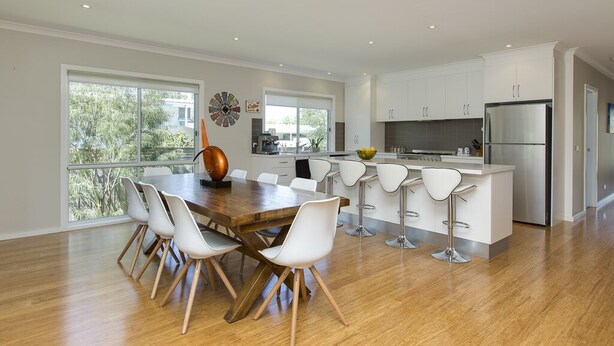 A modern kitchen with white cabinets, a stainless steel refrigerator, and a dining area with a wooden table and white chairs. - Beautiful Vibe Energy Escape Lux w Bonuses Phillip Island 100m to nature inlet (Rhyll)