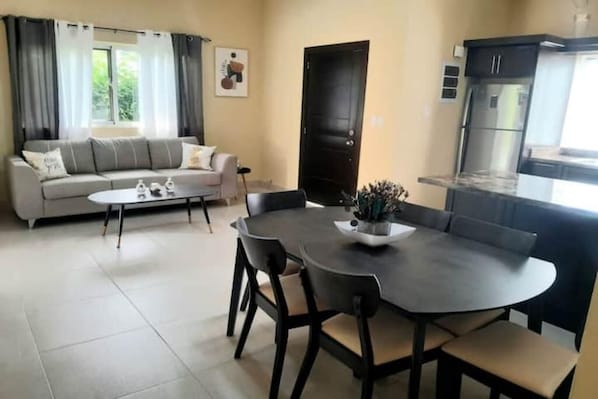 Un salon moderne comprenant un canapé, une table basse et une table à manger avec des chaises. Il y a également un coin cuisine avec un réfrigérateur et des placards.