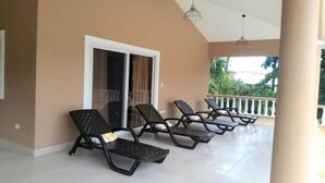 A covered outdoor area with four lounge chairs and a sliding glass door.