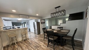 Una cocina moderna con armarios blancos, un refrigerador de acero inoxidable y un comedor con mesa y sillas de madera.