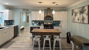 Una cocina amplia con una isla central, taburetes blancos de bar e iluminación colgante.