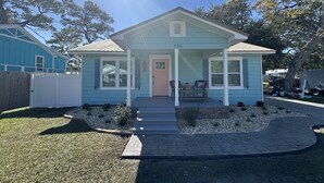 Una casa de un piso color azul claro, con un porche delantero, una puerta rosa y el número '434' en la fachada.