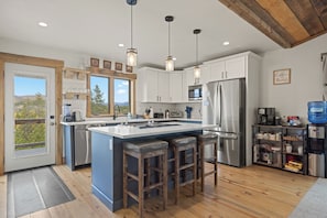 A modern kitchen with a central island, stainless steel appliances, and a view through the window.