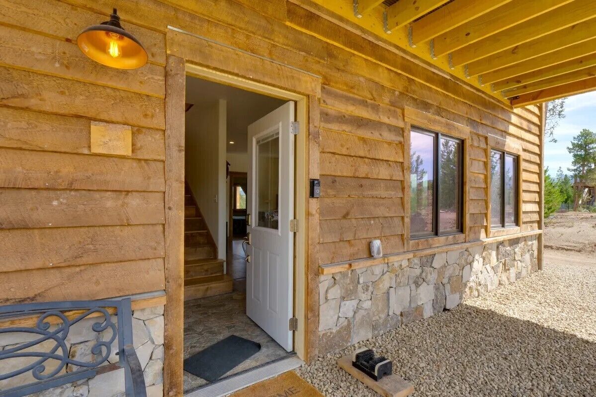 Una cabaña de madera con chimenea de piedra, una puerta que da al interior y un camino de entrada de grava.