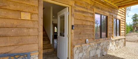 Una cabaña de madera con chimenea de piedra, una puerta que da al interior y un camino de entrada de grava.
