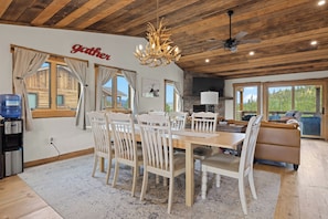A dining area with a wooden table and chairs, a chandelier, and a stone fireplace.